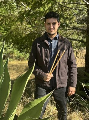 Man holding drumsticks behind agave leaves.  