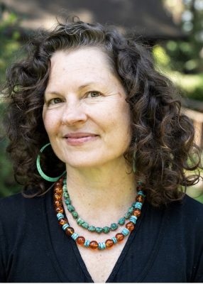 Portrait of Lavender Grace Kent with brown curly sholderlength hair, turqoiuse hoop earrings and amber and turqoise necklace 